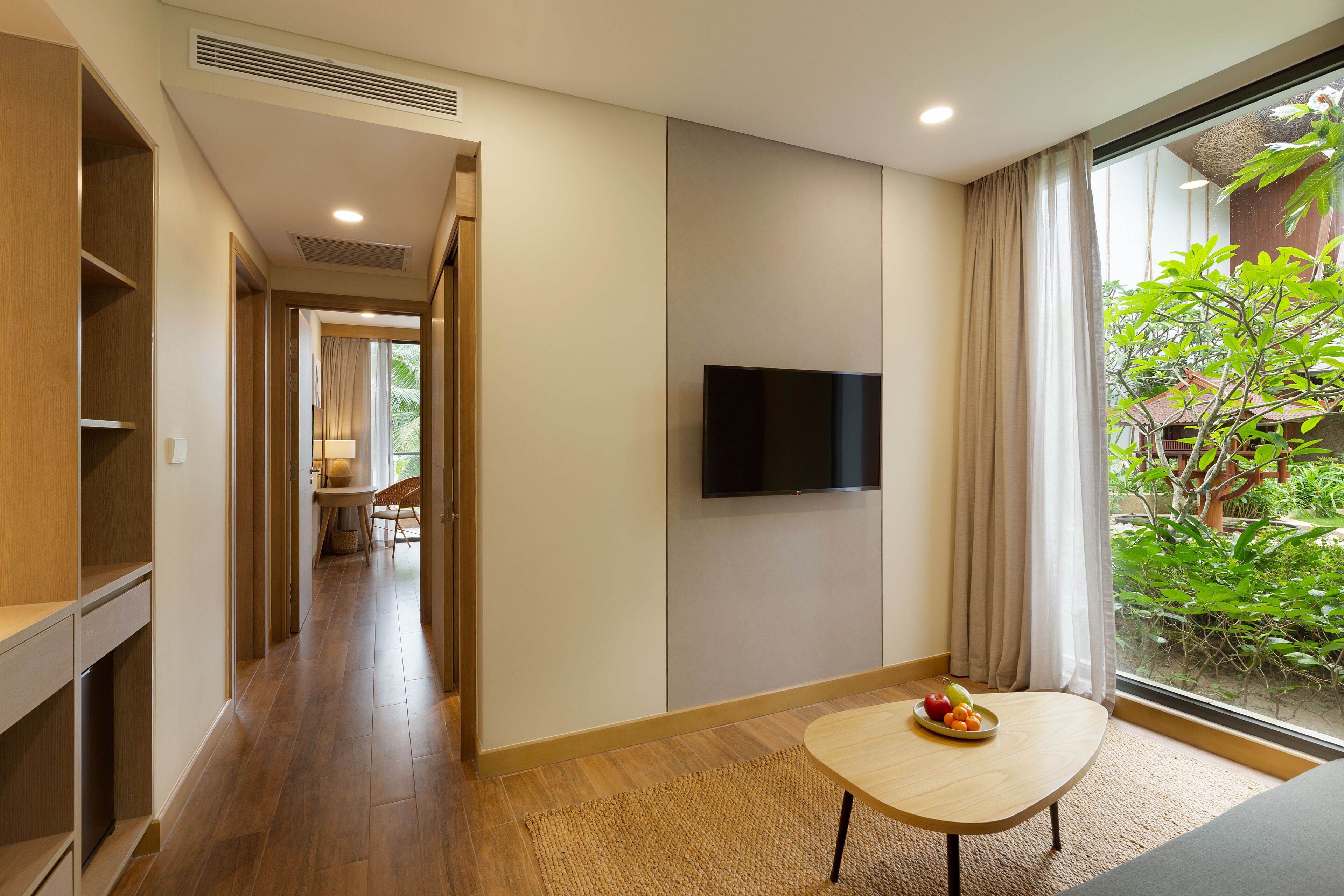 Habitación de hotel con piso de madera, televisor montado en la pared, una mesita con fruta y vista a zonas verdes.