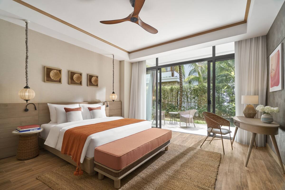 Une chambre d’hôtel moderne dotée d’un grand lit, d’un ventilateur de plafond, d’une vue sur l’extérieur et d’un petit coin salon avec une table et des chaises.