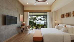 Habitación de hotel moderna con una cama grande, un televisor de pantalla plana, una zona de comedor con mesa y sillas, y vistas a palmeras a través de amplios ventanales.