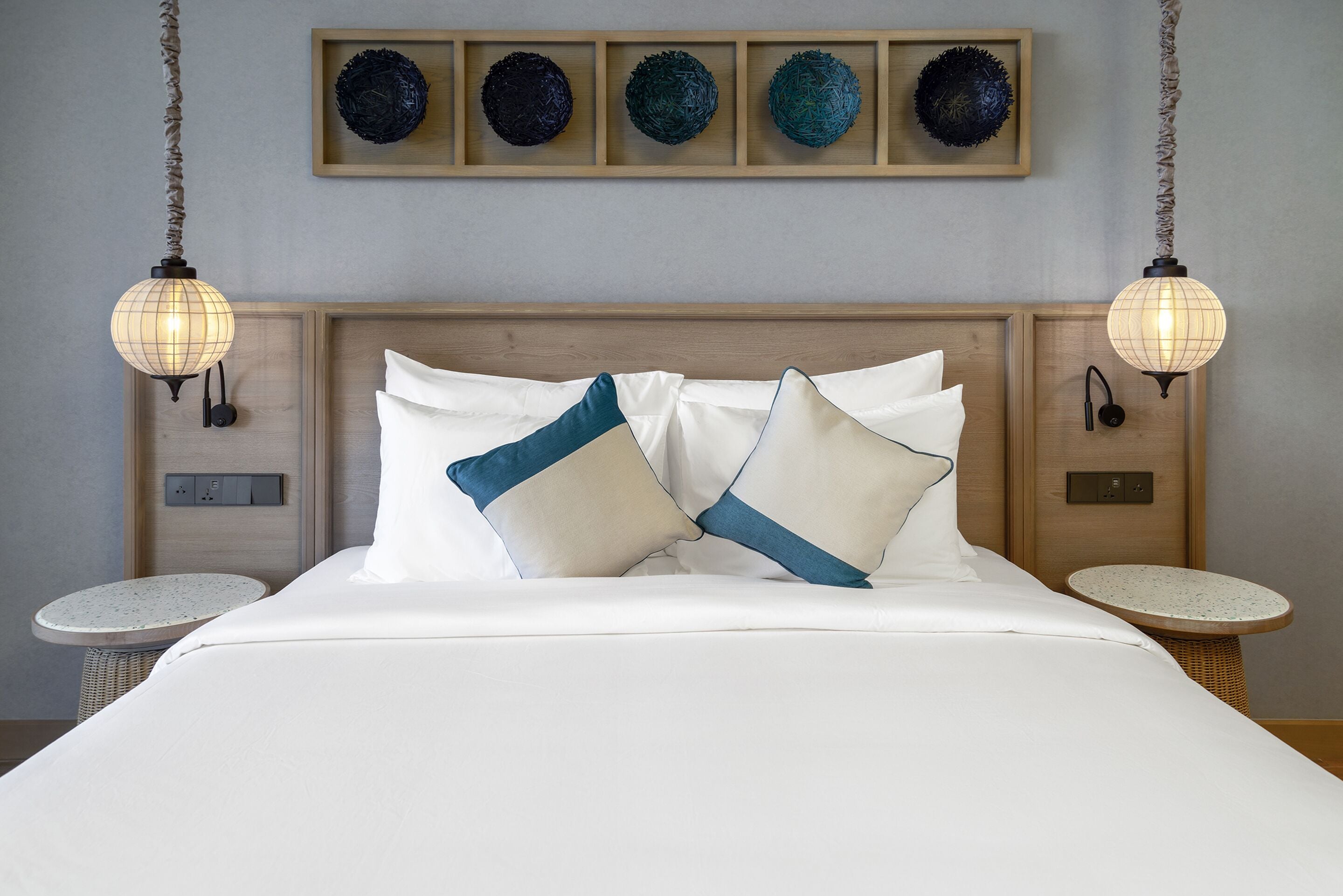 A neatly made bed with white and blue pillows, a wooden headboard, and two wall-mounted lamps.