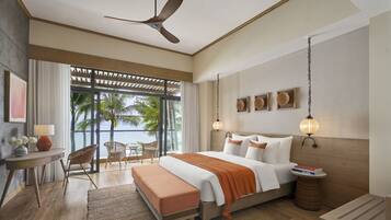 A modern hotel room with a large bed, a ceiling fan, a balcony with a view of palm trees, and a desk with a lamp.