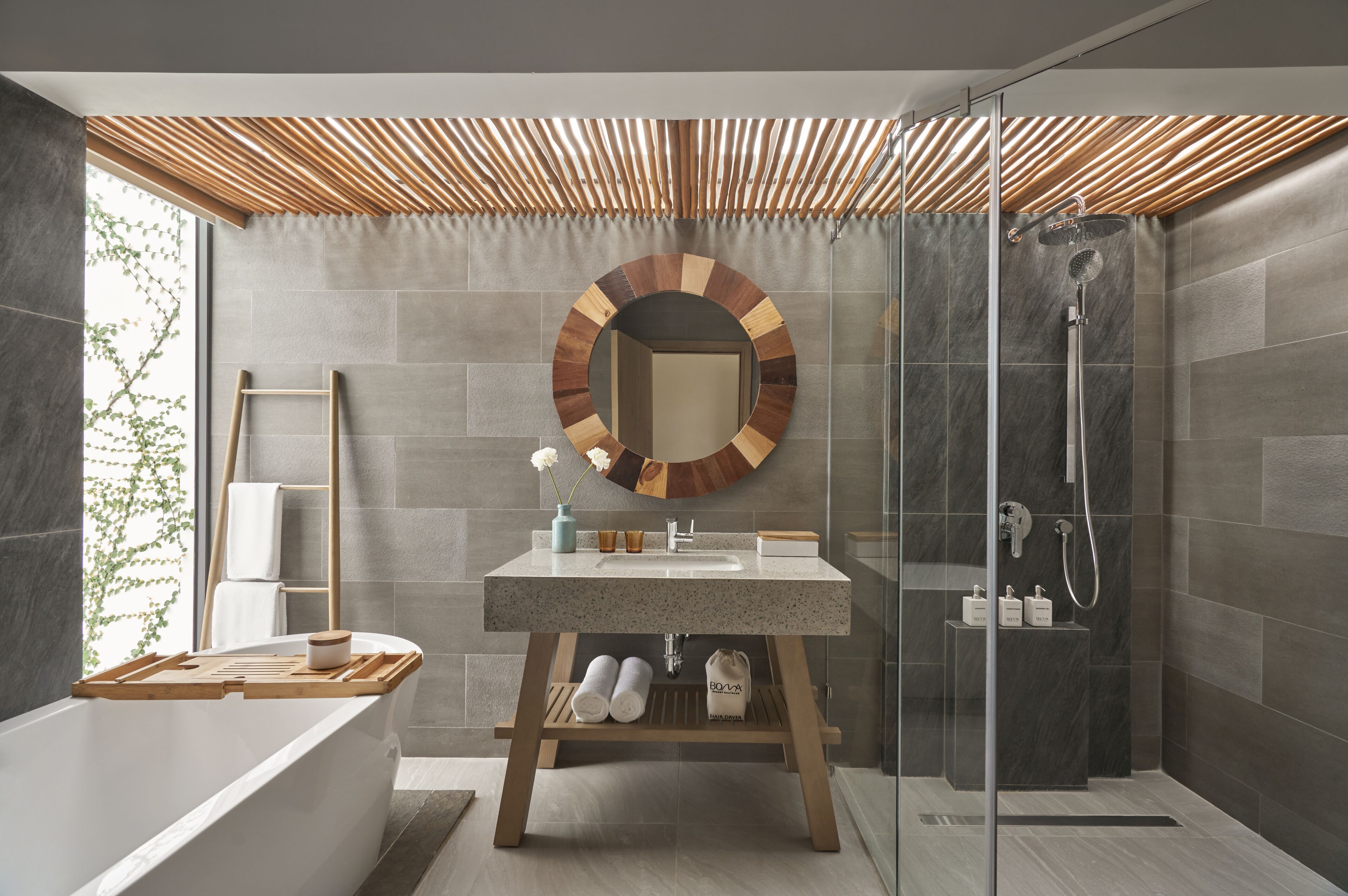 A modern bathroom with a freestanding bathtub, a round mirror, a shower, and a vanity with a sink and towel rack.