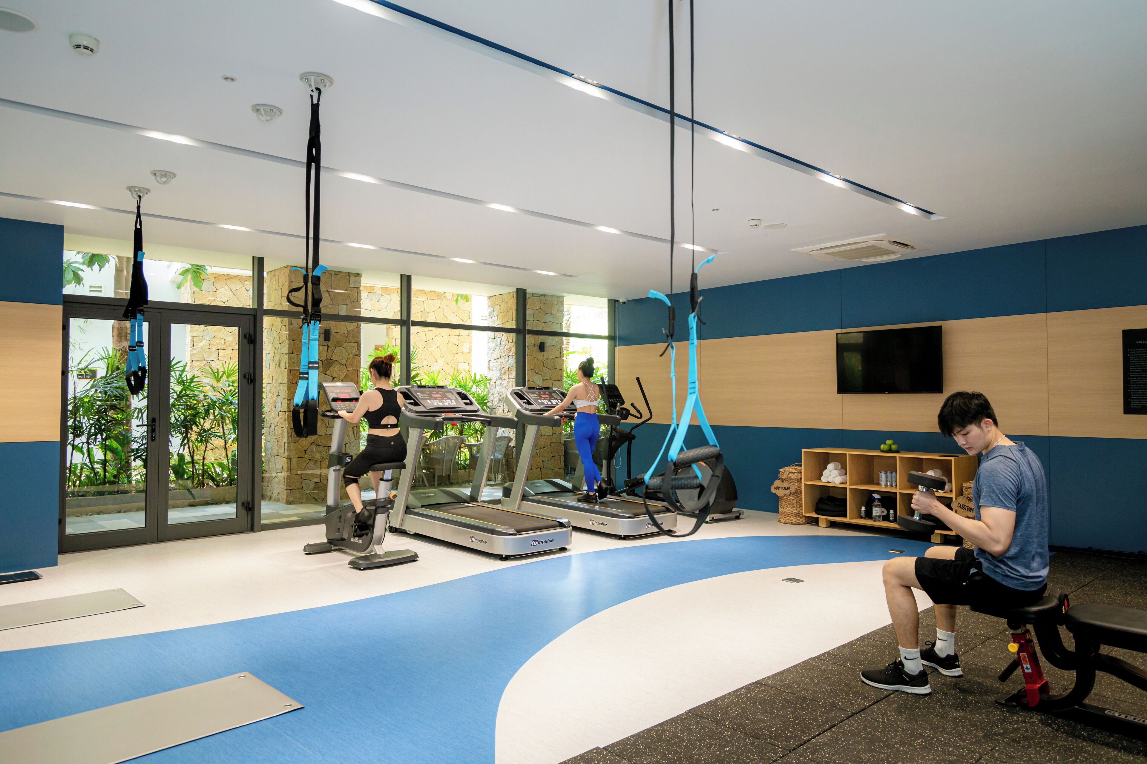 A gym with treadmills, a stationary bike, and a yoga ball. There is a bench and a shelf with items on it.