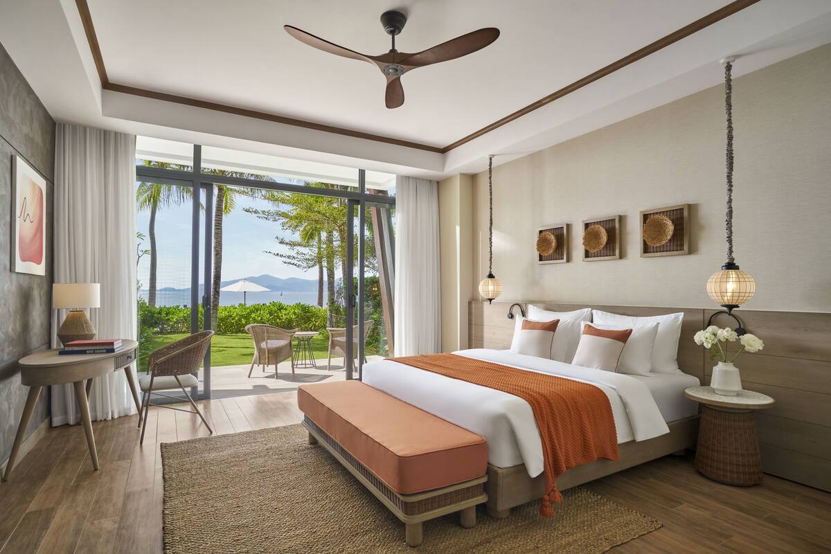 Une chambre d’hôtel moderne dotée d’un grand lit, d’un ventilateur de plafond, d’une vue sur l’extérieur et d’un petit coin salon avec une table et des chaises.