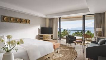 Una moderna camera d'albergo con un letto grande, una televisione, un'area salotto con vista sul mare e un balcone con vista sulle montagne.
