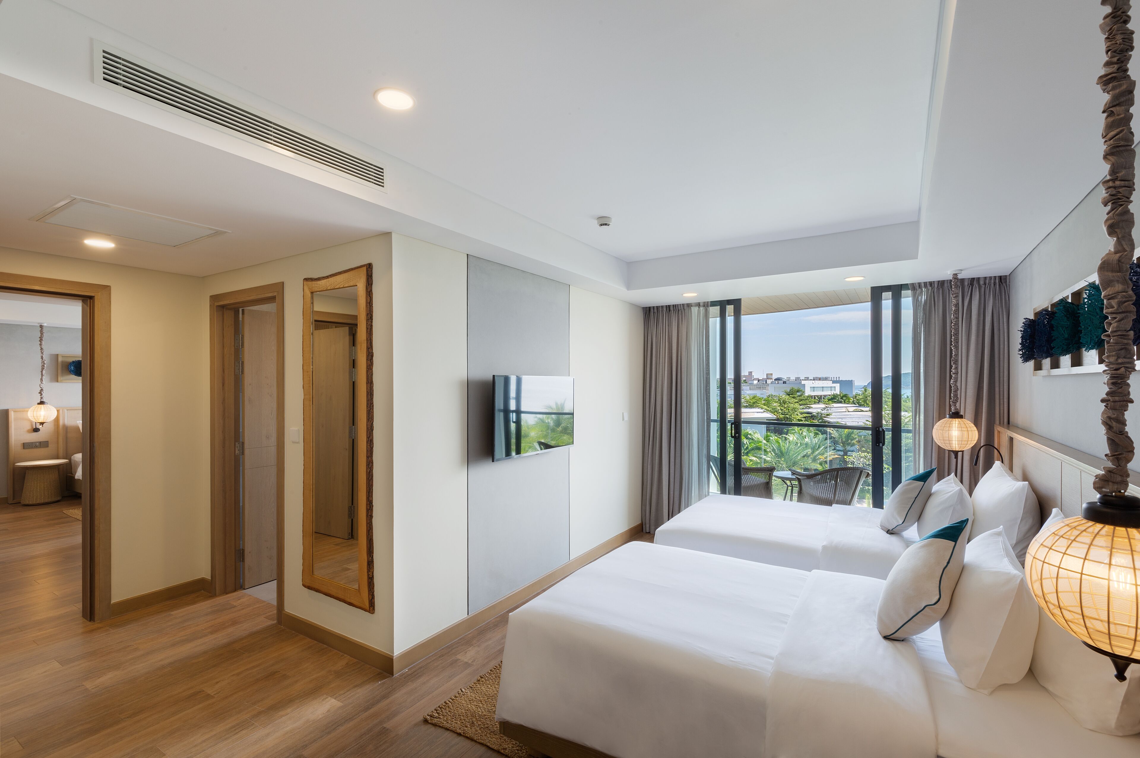 A hotel room with two beds, a TV, a large window with curtains, and a city view.