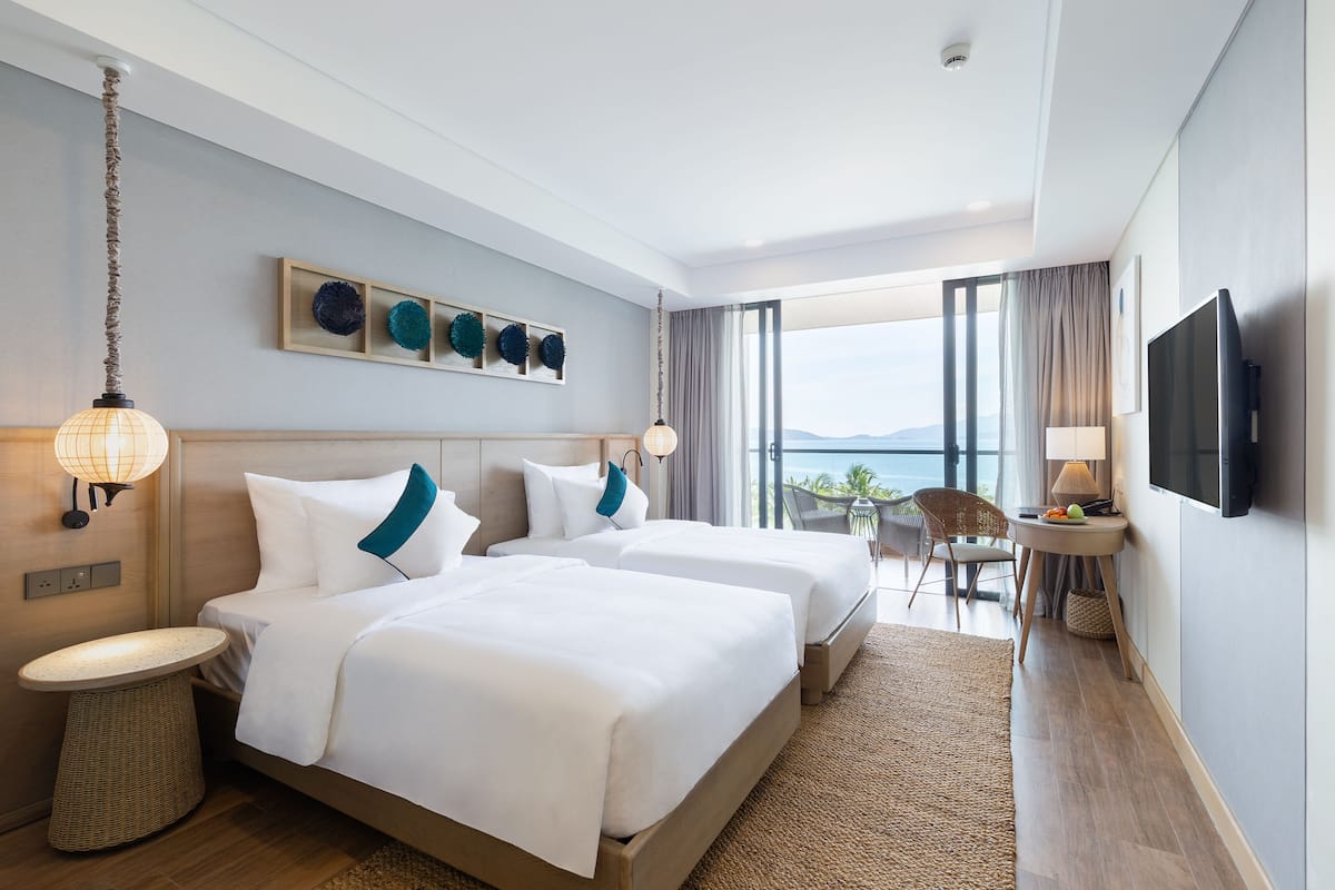 Une chambre d’hôtel avec deux lits, une télévision, un balcon avec vue et un coin repas.