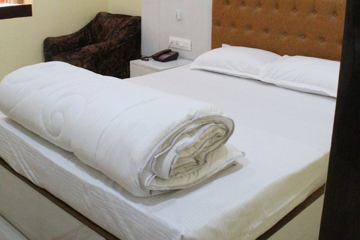 Una habitación de hotel con cama, mesita de noche, teléfono y una silla.