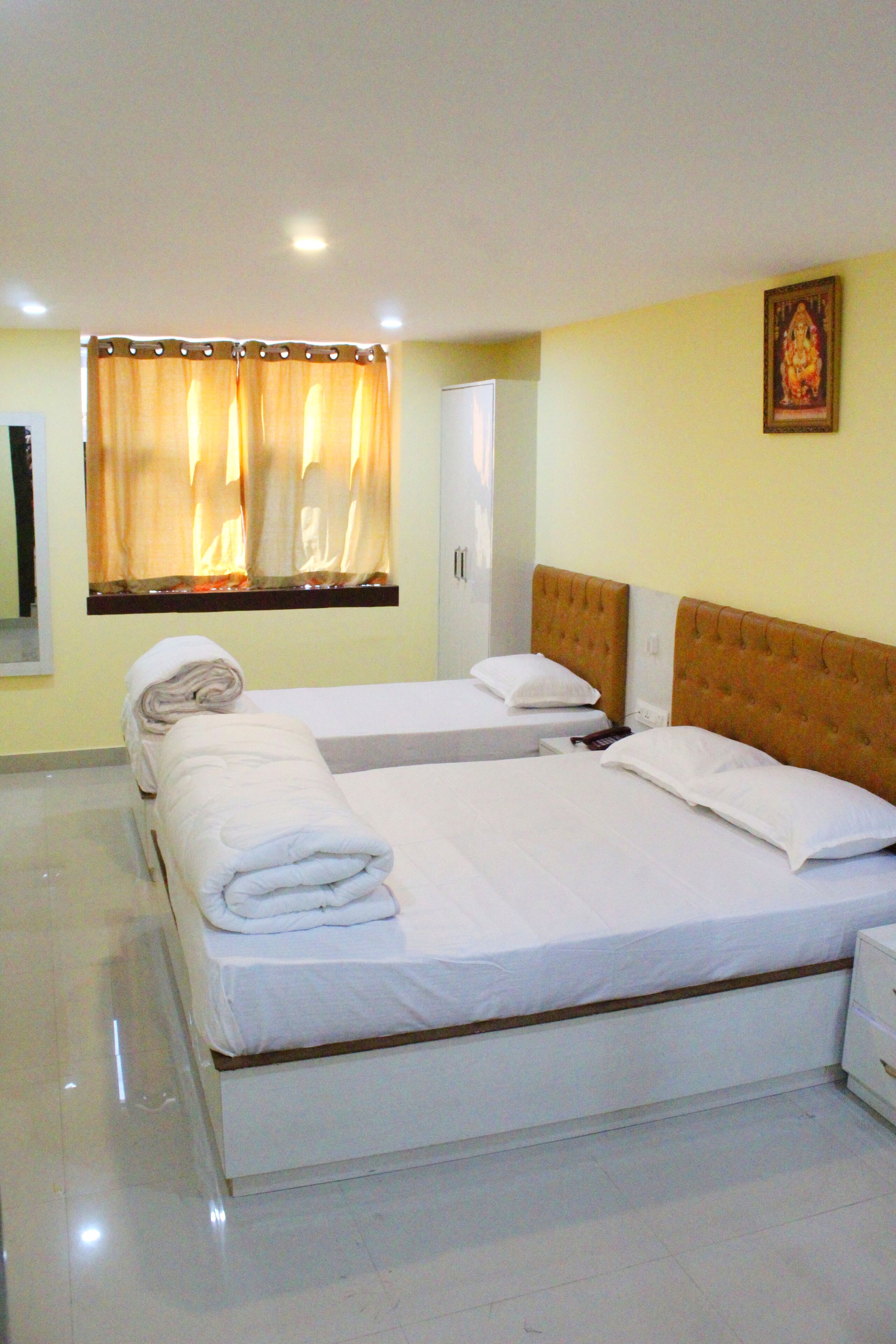 A hotel room with a large bed, a bedside table, a nightstand, a window with curtains, and a wall-mounted picture.