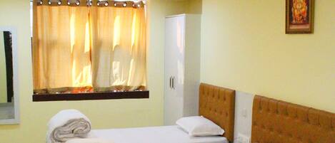 A hotel room with a large bed, a bedside table, a nightstand, a window with curtains, and a wall-mounted picture.