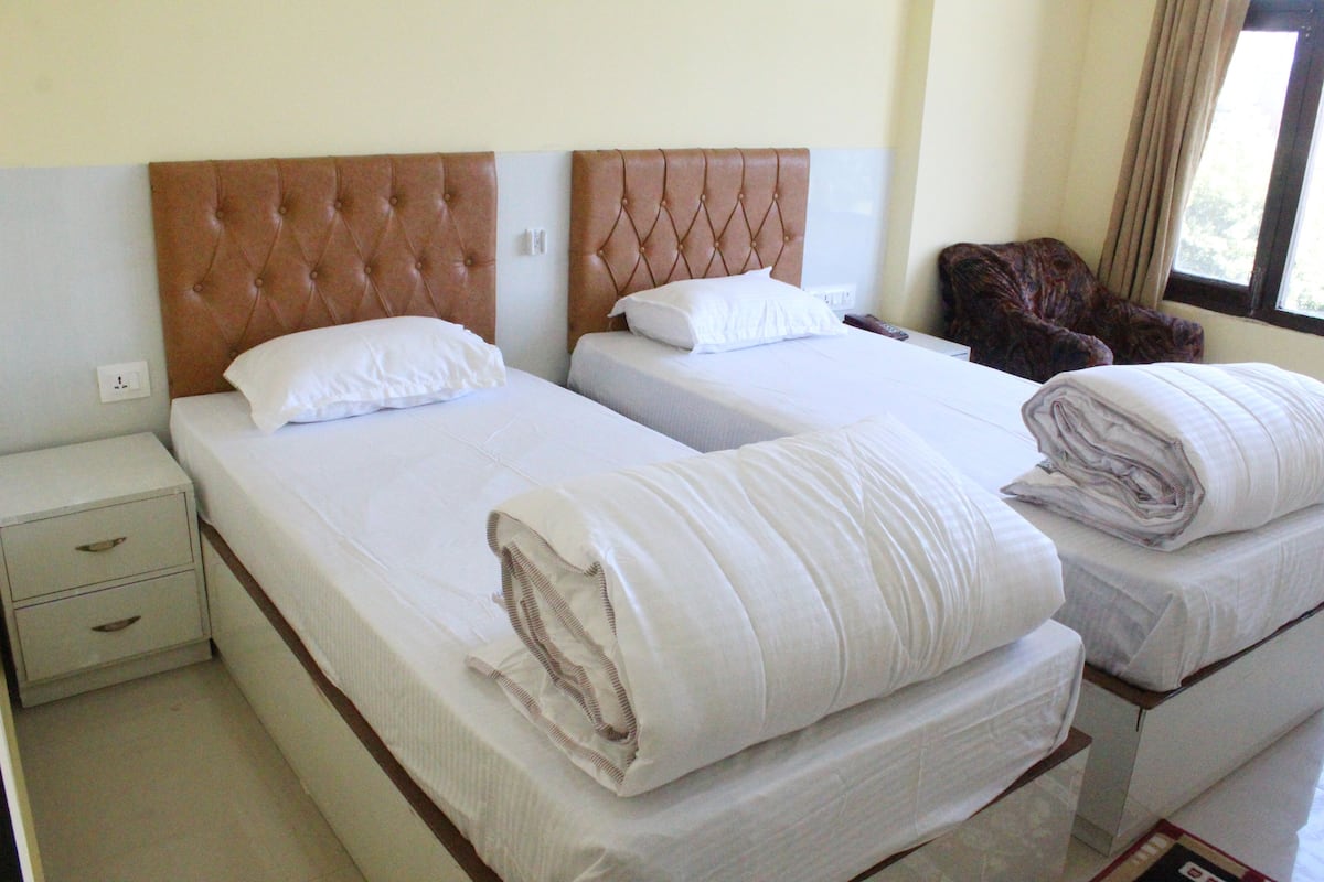 Habitación de hotel con dos camas, cada una con cabecero capitonado, ropa blanca y una manta doblada con cuidado al lado.