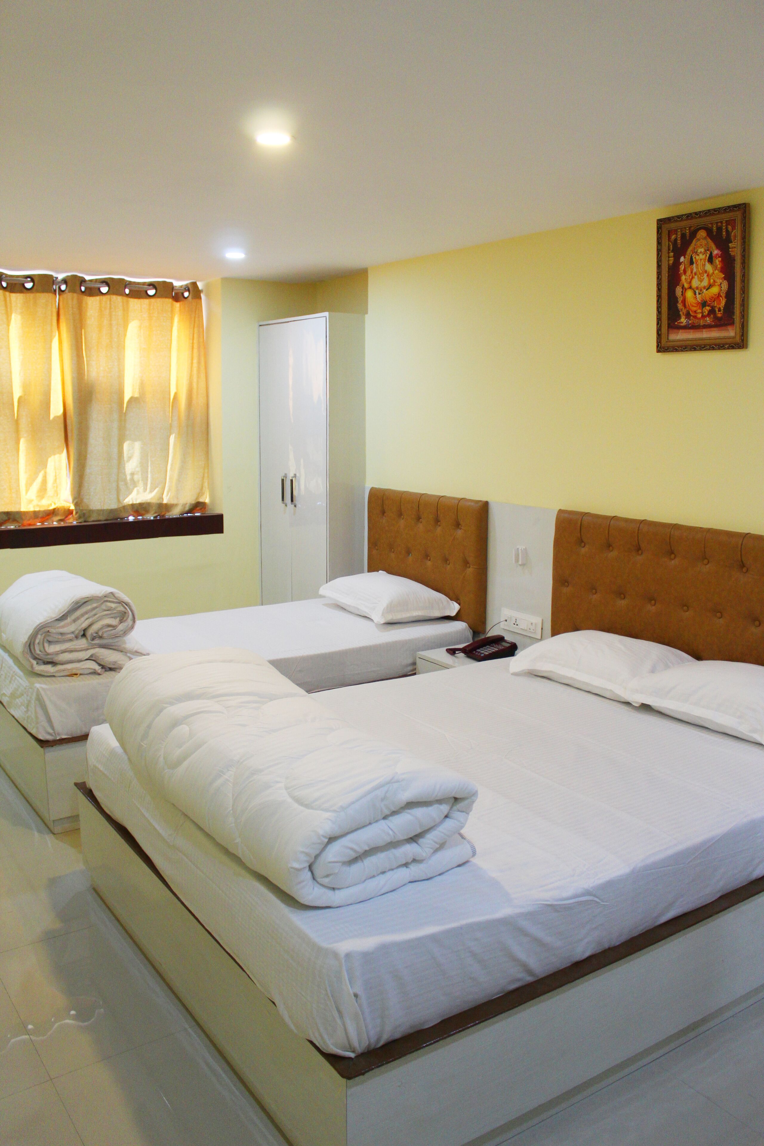 A hotel room with two beds, a wardrobe, a window with curtains, and a wall-mounted picture.