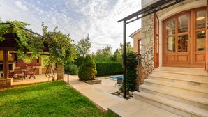 Una casa de piedra con una escalera de madera que lleva a una puerta, una piscina y un patio con mobiliario exterior.