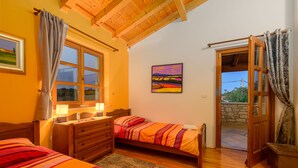 Un dormitorio con dos camas, un aparador, una ventana con cortinas, un cuadro en la pared y una puerta abierta que da al exterior.