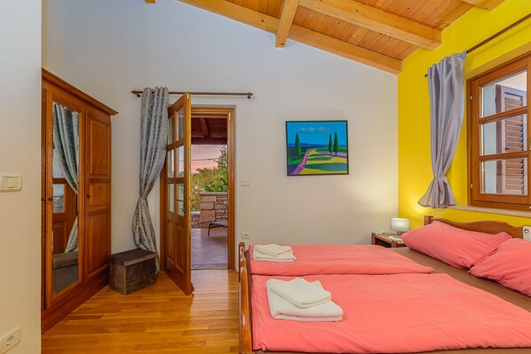 A room with two beds, wooden flooring, a painting on the wall, and a view through an open door. - Villa Aurelia (Istria - Pajkovići) (Pajkovići)