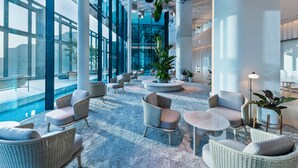 A spacious lobby with high ceilings, large windows, and a central seating area with wicker chairs and tables.