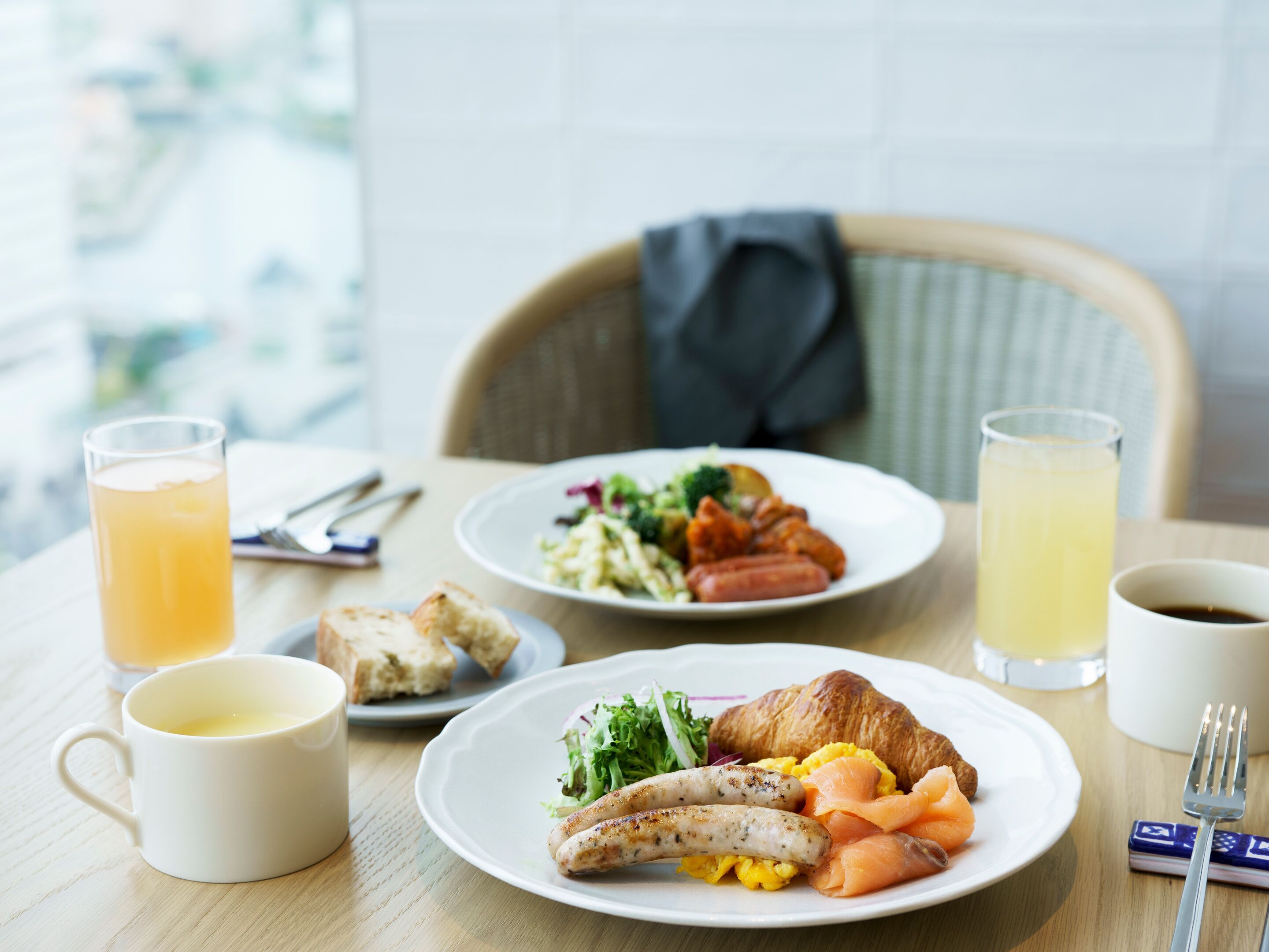 Una mesa con platos de comida, un croissant y bebidas.