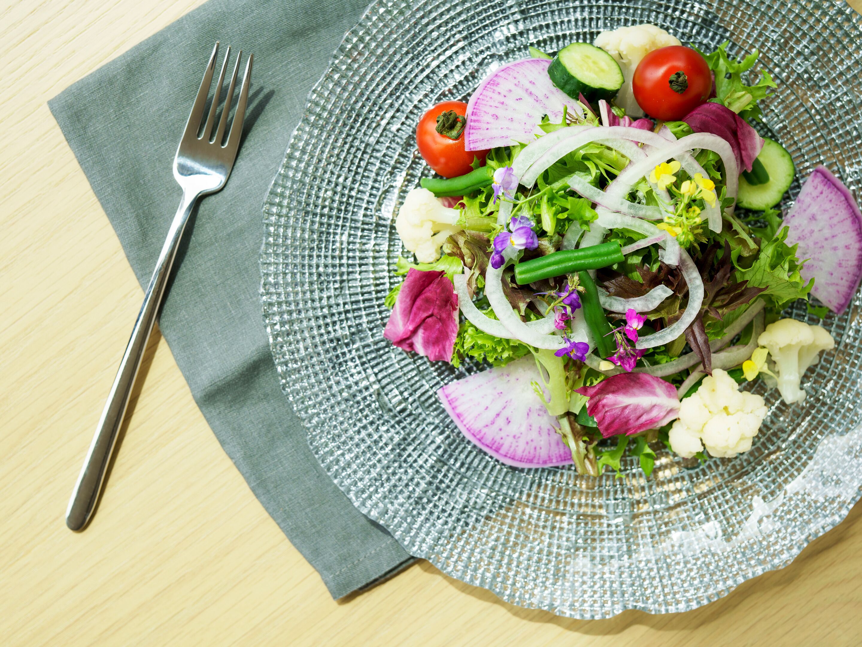En salat med forskellige grøntsager og en gaffel på en serviet.