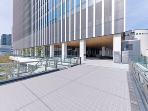 Ein modernes Gebäude mit einer Glasfassade und einem überdachten Außenbereich mit Fliesenboden und Metallgeländern.