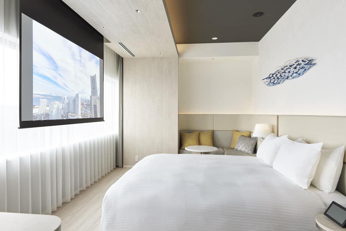 A modern hotel room with a large bed, a small round table, and a city view through the window.
