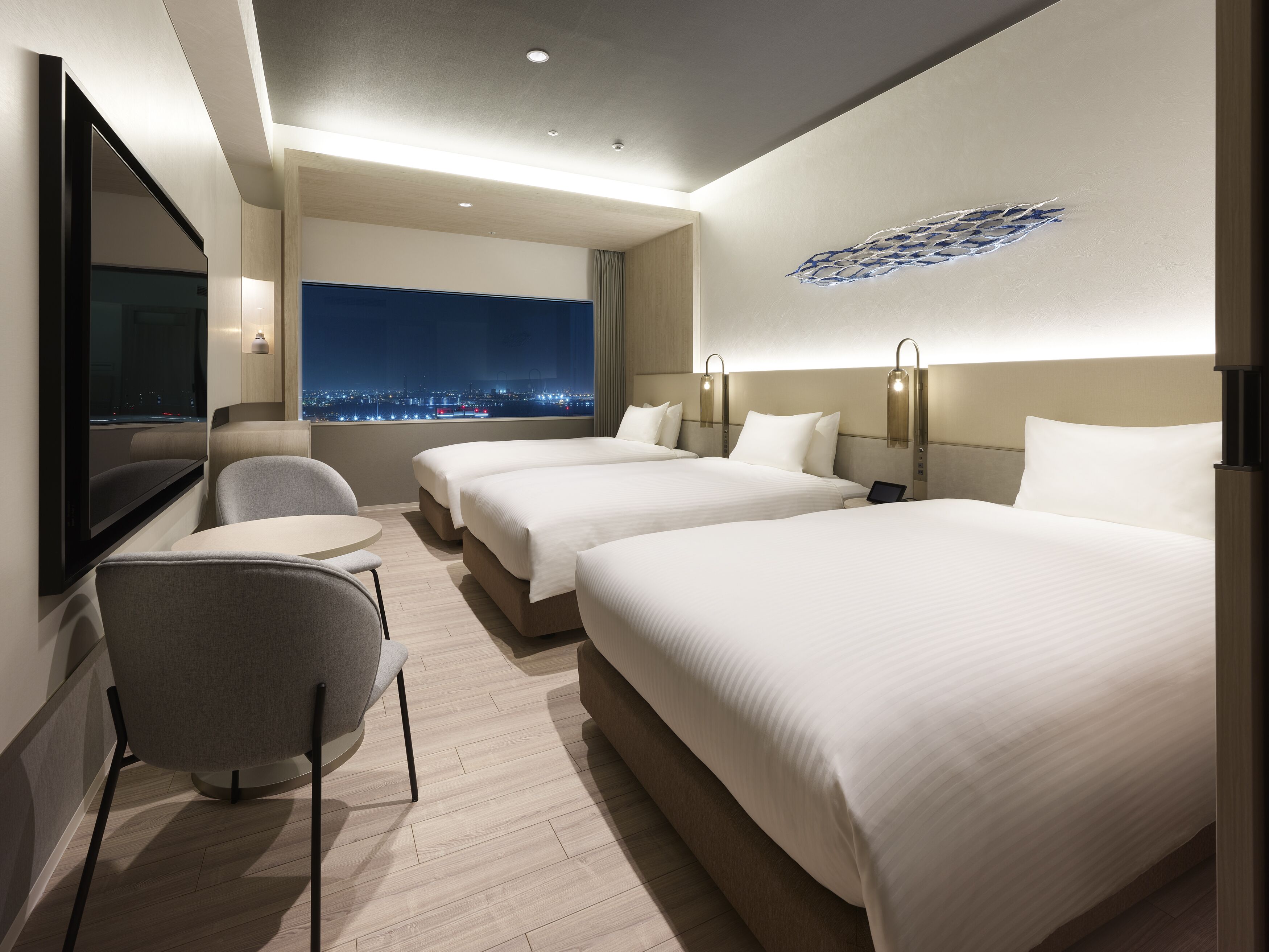 A hotel room with two beds, a TV, a desk, and a city view.