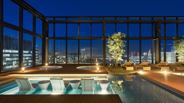 A rooftop infinity pool with lounge chairs and a view of the cityscape at night.