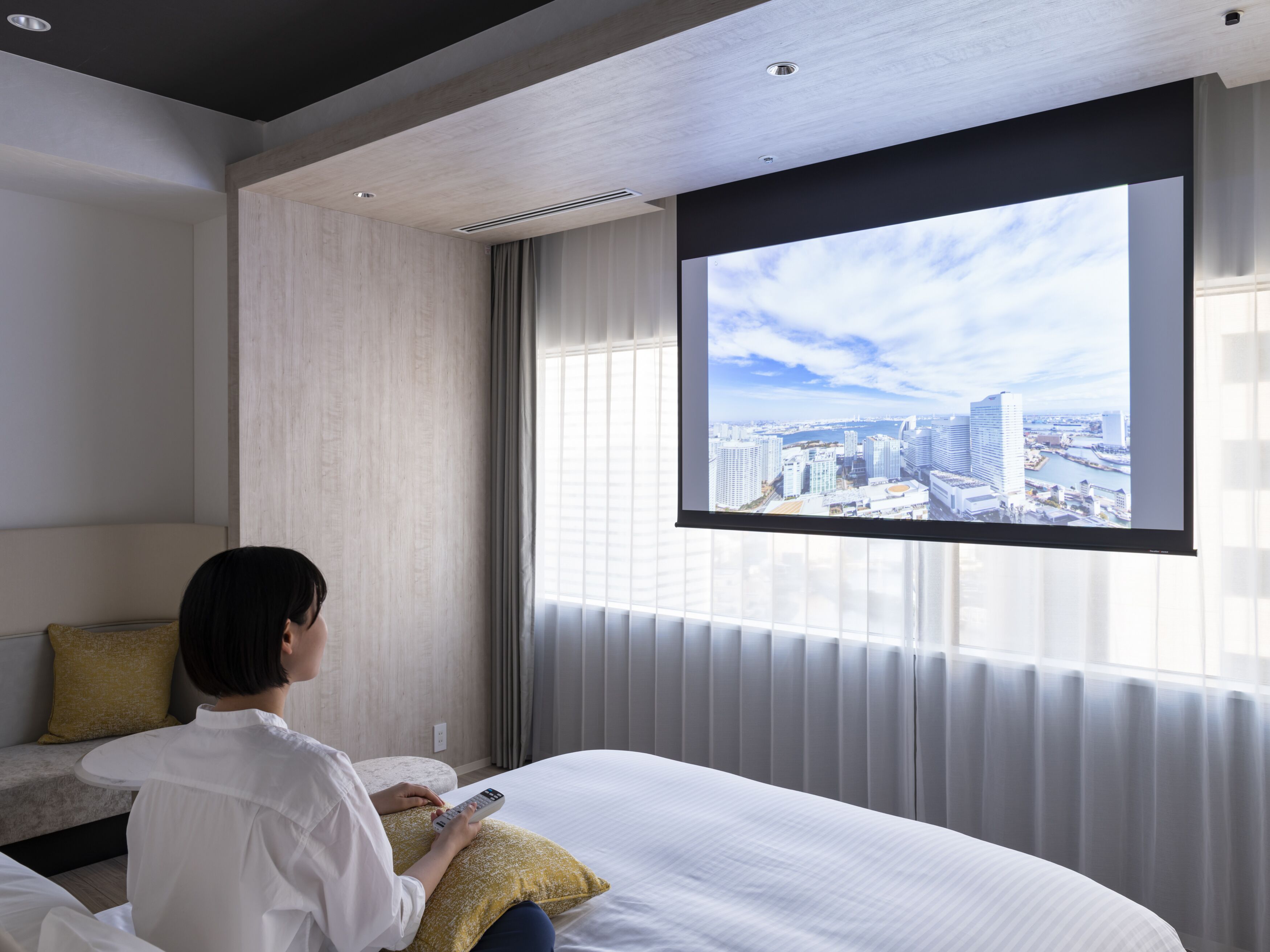 A hotel room with a bed, a large window, and a cityscape view.