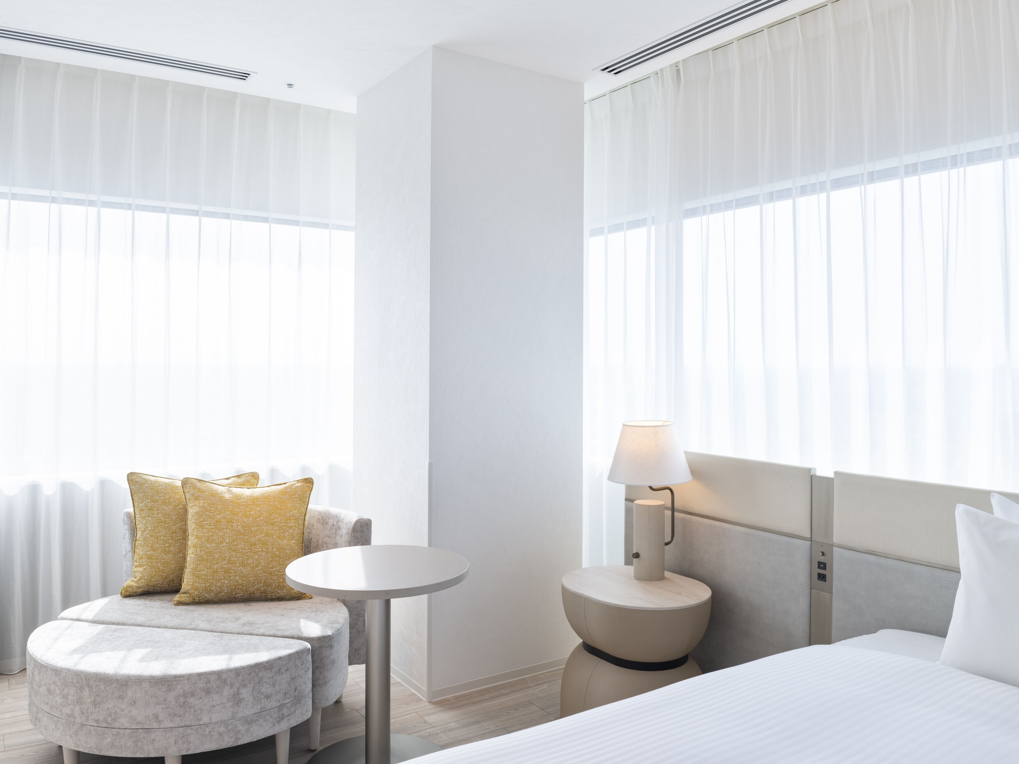 A hotel room with a bed, a round table, a small sofa with cushions, and a lamp.