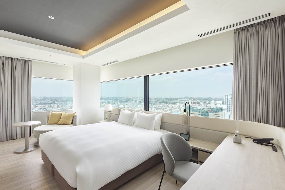 A modern hotel room with a large bed, a desk, and a view of the city.
