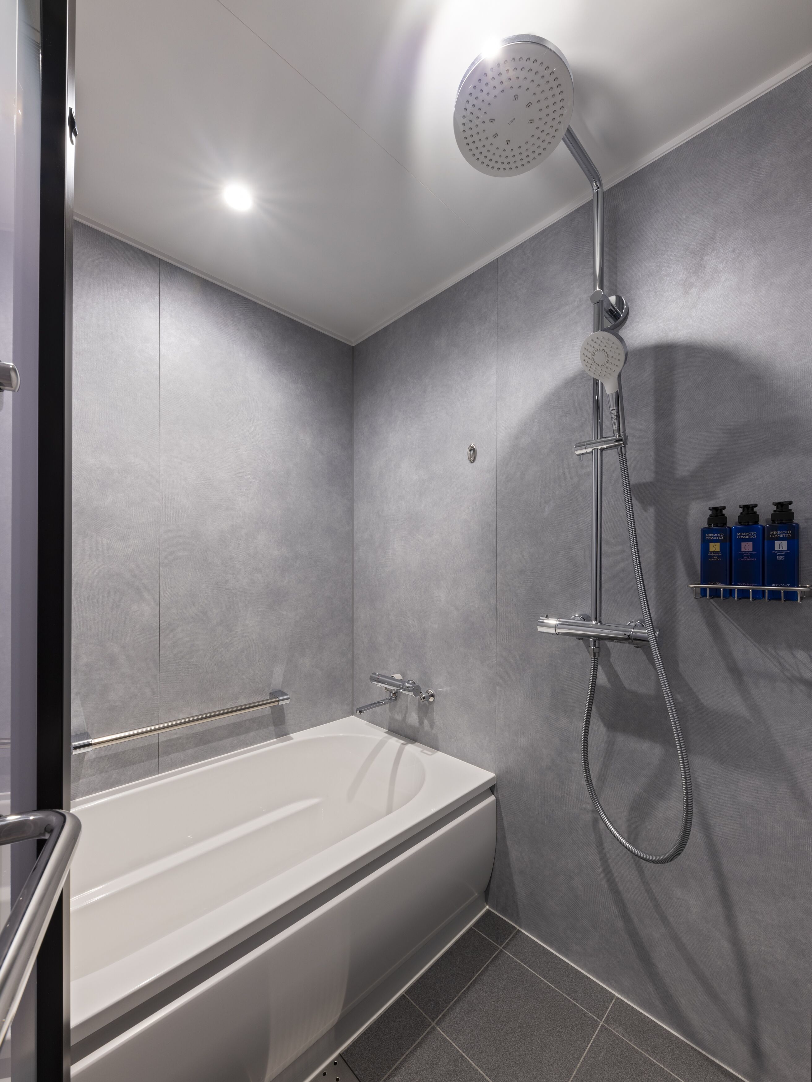 A modern bathroom with a bathtub, a shower with a handheld showerhead, and a wall-mounted soap dispenser.