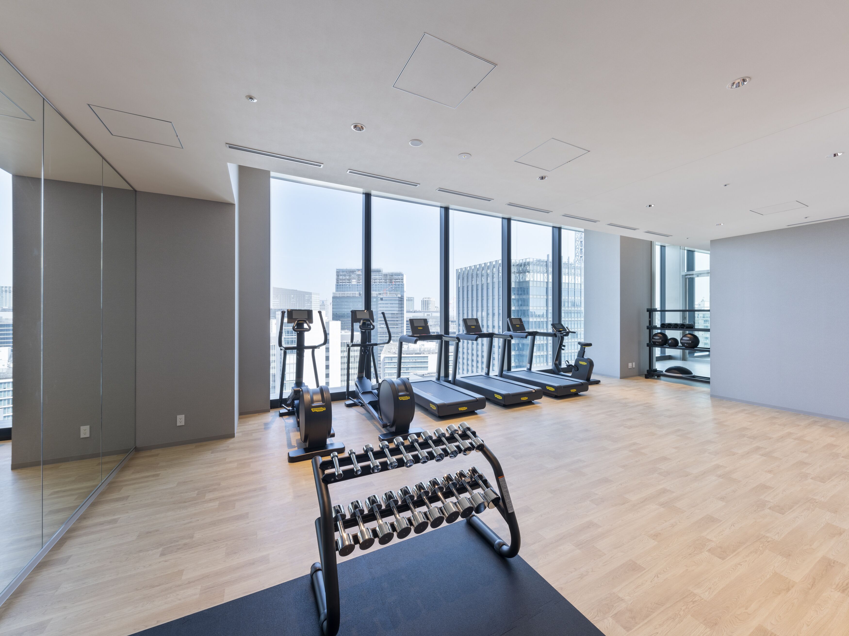 A modern gym with exercise equipment, large windows, and a city view.