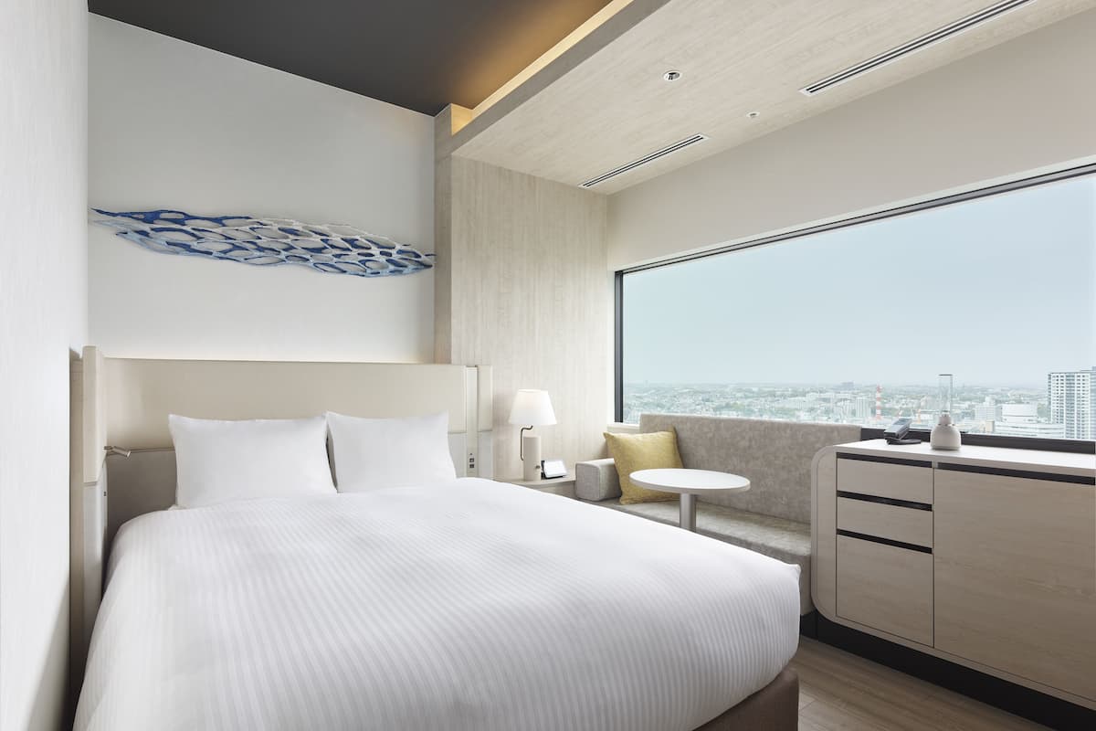 A modern hotel room with a large bed, a small table, a sofa, and a view of the city.