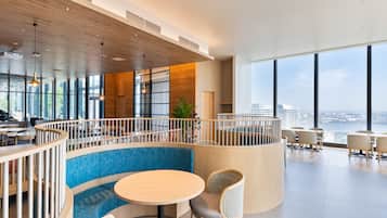 Una hall d'albergo moderna con un'area salotto dalle linee curve, una piscina e ampie finestre con vista sulla città.