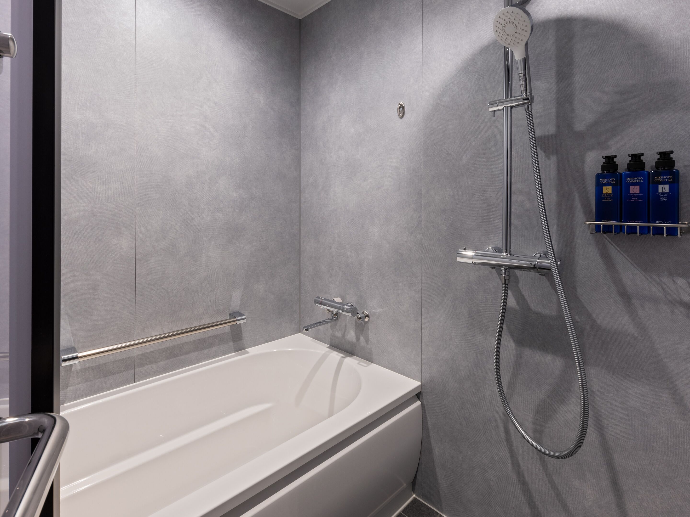 Un baño moderno con una bañera blanca, un cabezal de ducha manual y un dispensador de jabón de pared.