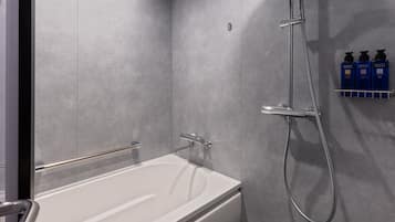 A modern bathroom with a white bathtub, a handheld showerhead, and a wall-mounted soap dispenser.