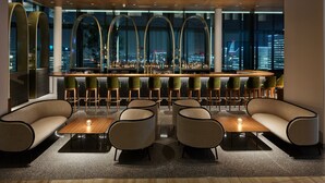 A modern bar area with a city view, featuring a bar counter, stools, and seating.