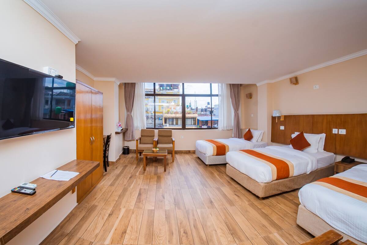 A hotel room with two beds, a TV, a desk, and a window with a city view.
