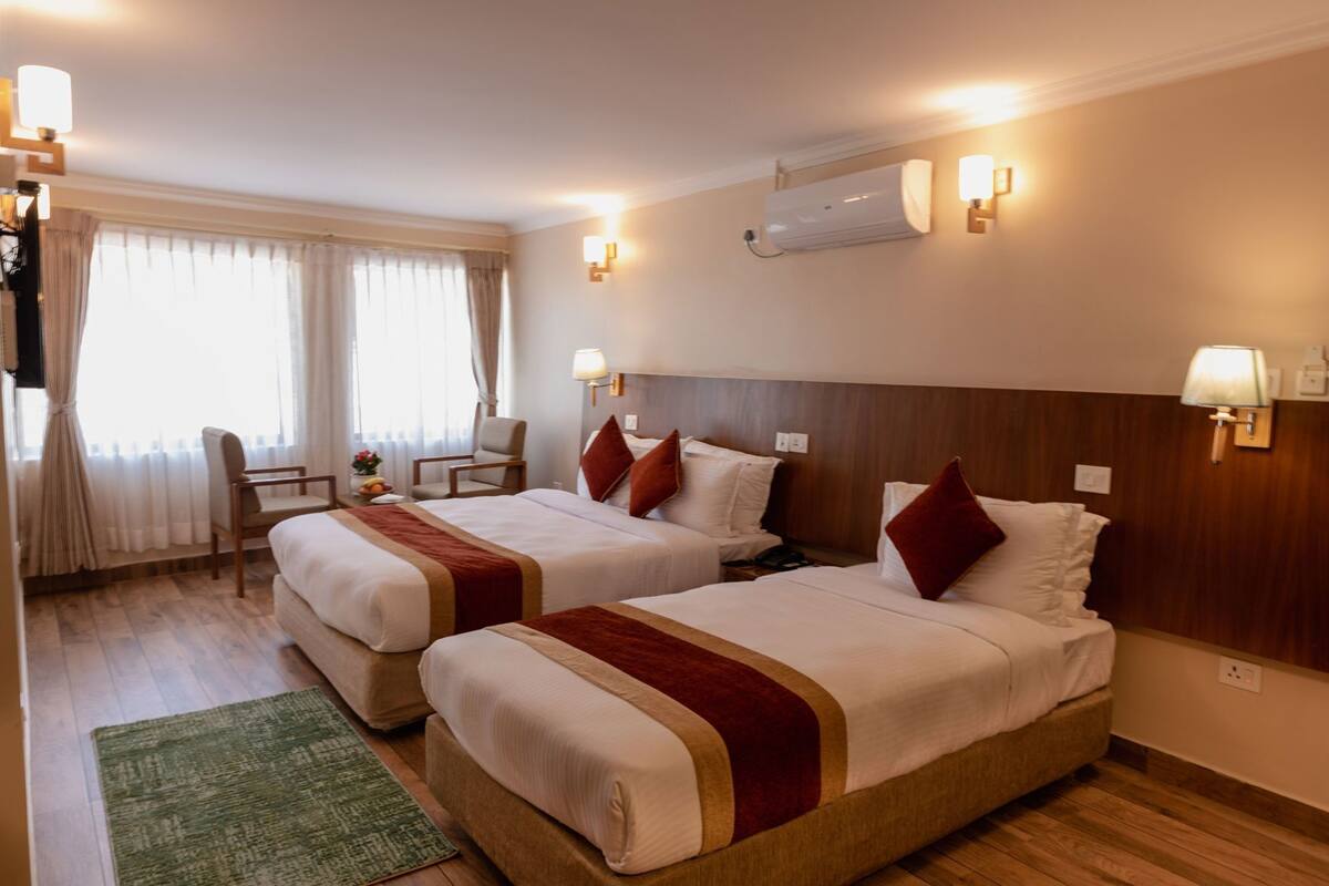 A hotel room with two beds, a desk, a chair, and a window with curtains.