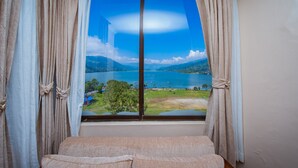 A room with a large window offering a view of a lake and mountains. - Hotel Fewa Camp (Pokhara)