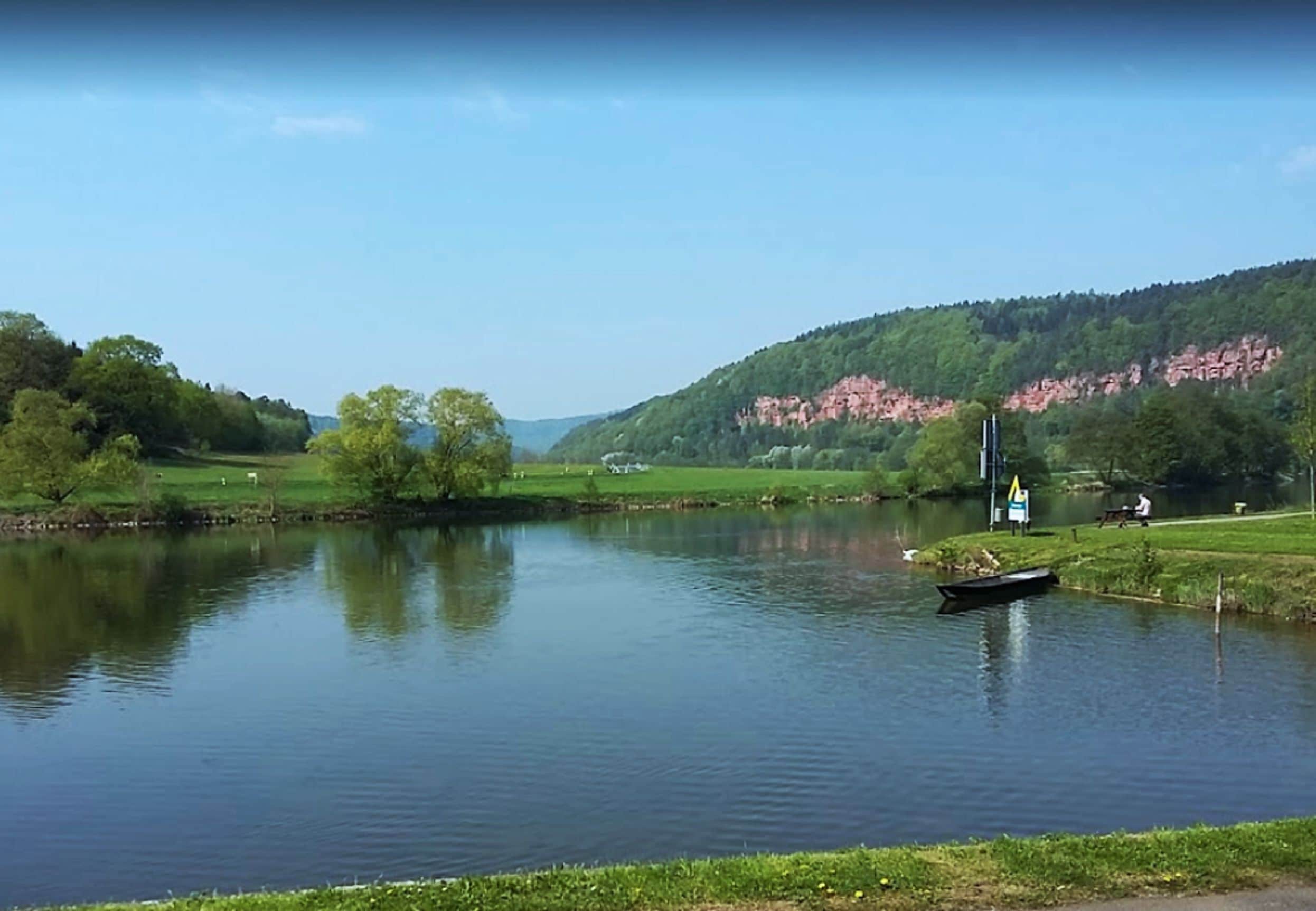 Ein ruhiger See mit einem Boot, umgeben von grünen Hügeln und einem klaren Himmel.