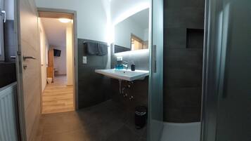 A modern bathroom with a white sink, dark tiles, and a visible shower area.