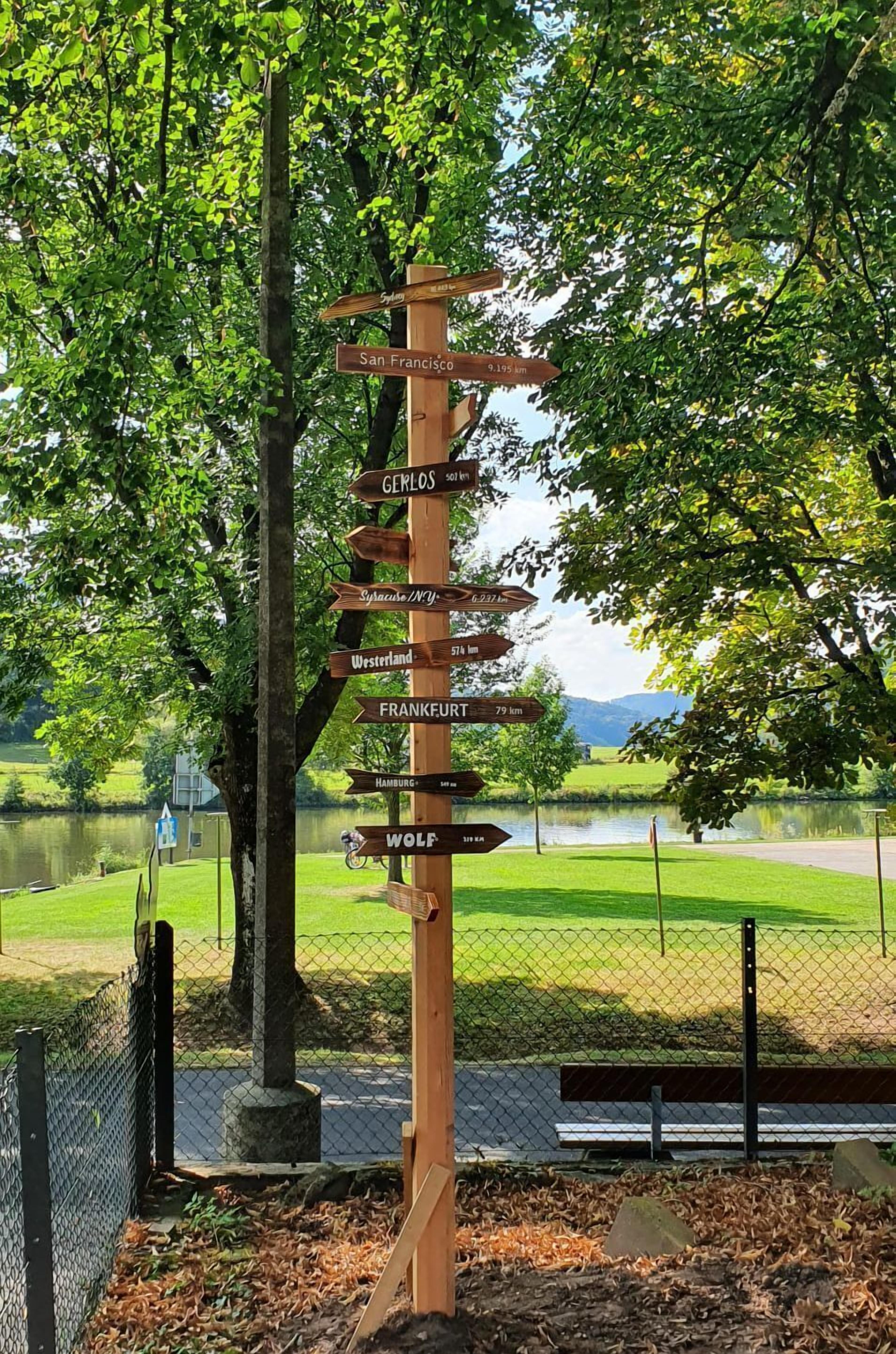 Un panneau indicateur en bois, orné de flèches indiquant les différentes villes et les distances correspondantes.