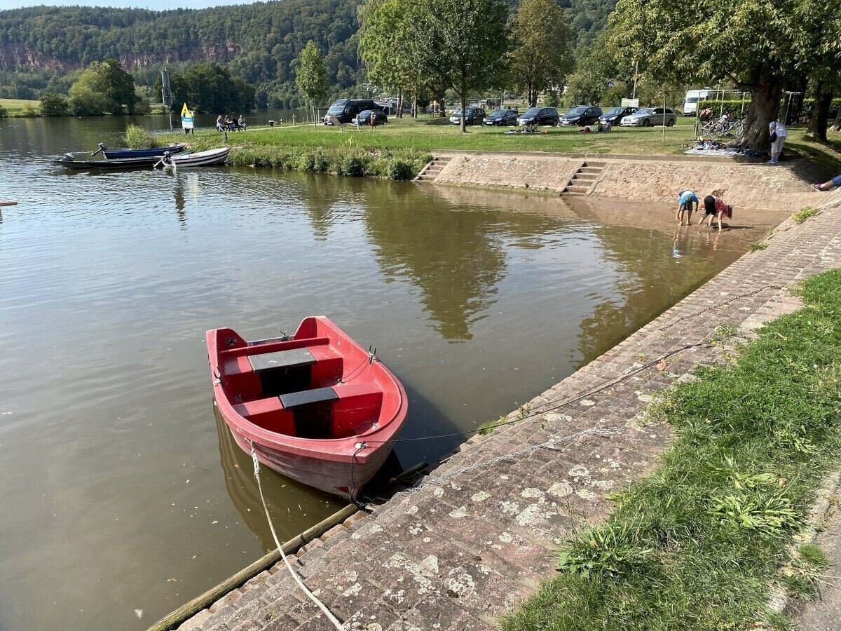 Een rustig meer met een rode boot afgemeerd aan de oever, omringd door grasvelden en bomen.