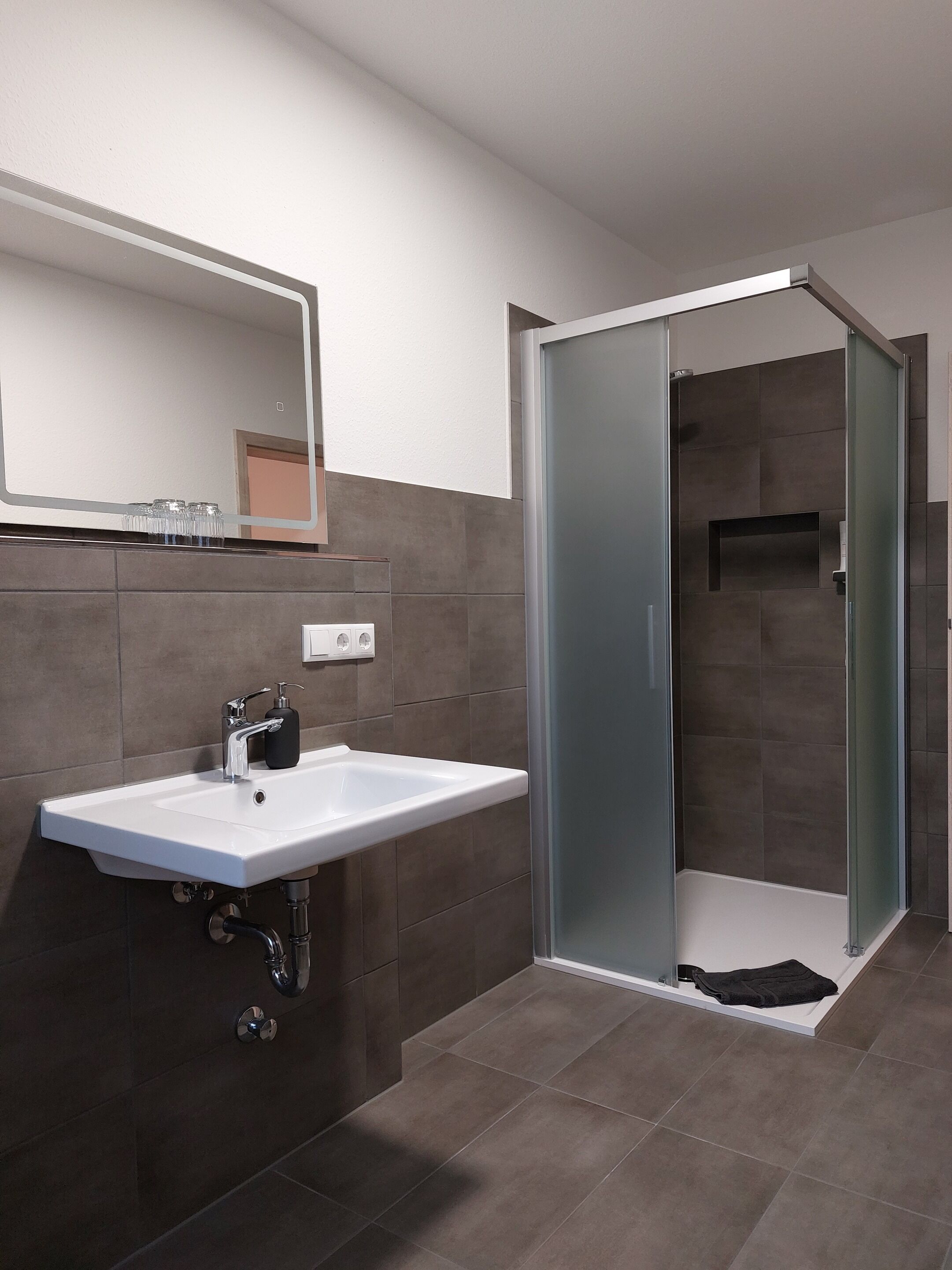A modern bathroom with a white sink, a mirror, and a glass-enclosed shower.