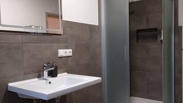 A modern bathroom with a white sink, a mirror, and a glass-enclosed shower.