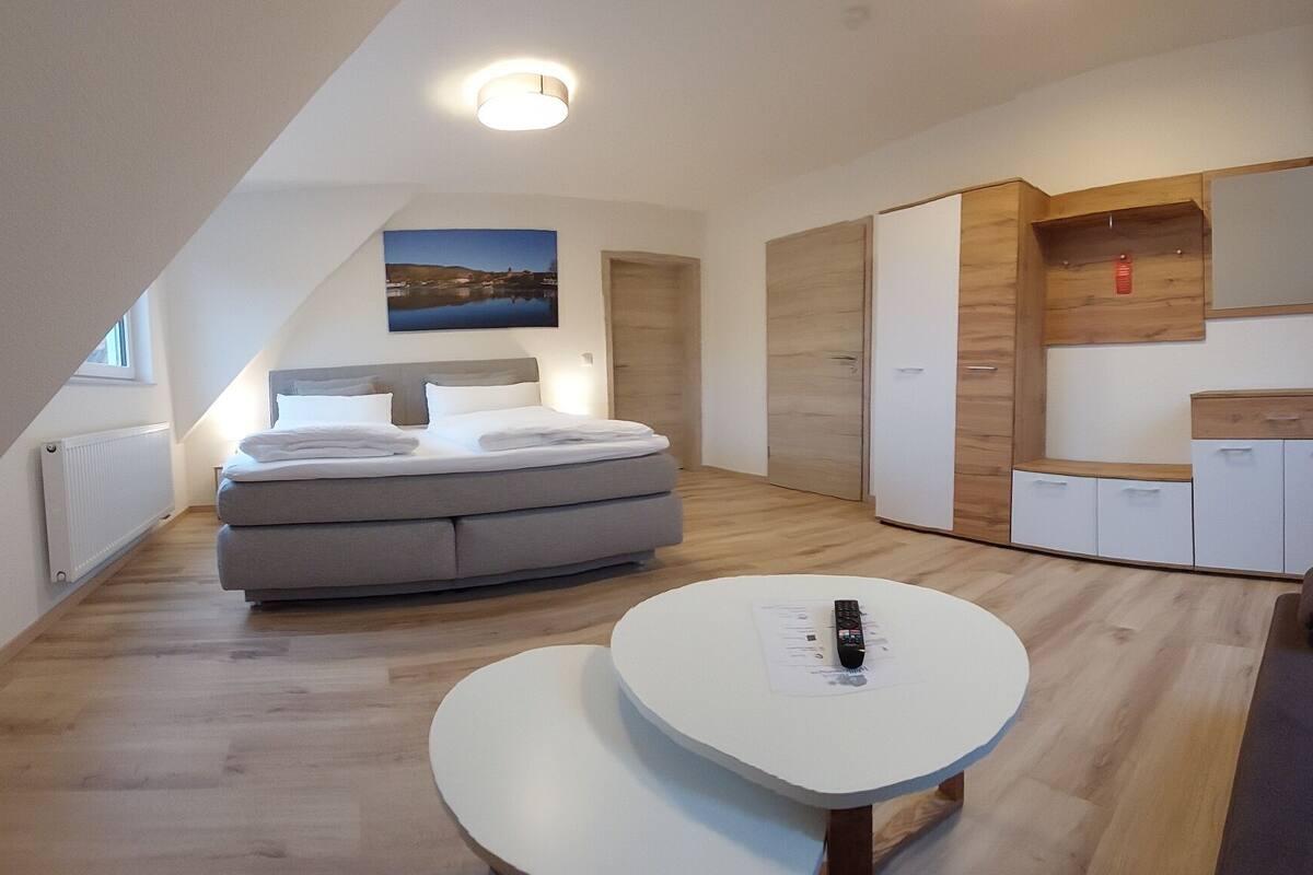 A modern, well-lit room with a bed, a sofa, a small table, and built-in wardrobes.