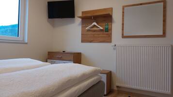 A bedroom with a bed, a dresser, a TV mounted on the wall, a radiator, and a window with a view of the outdoors.