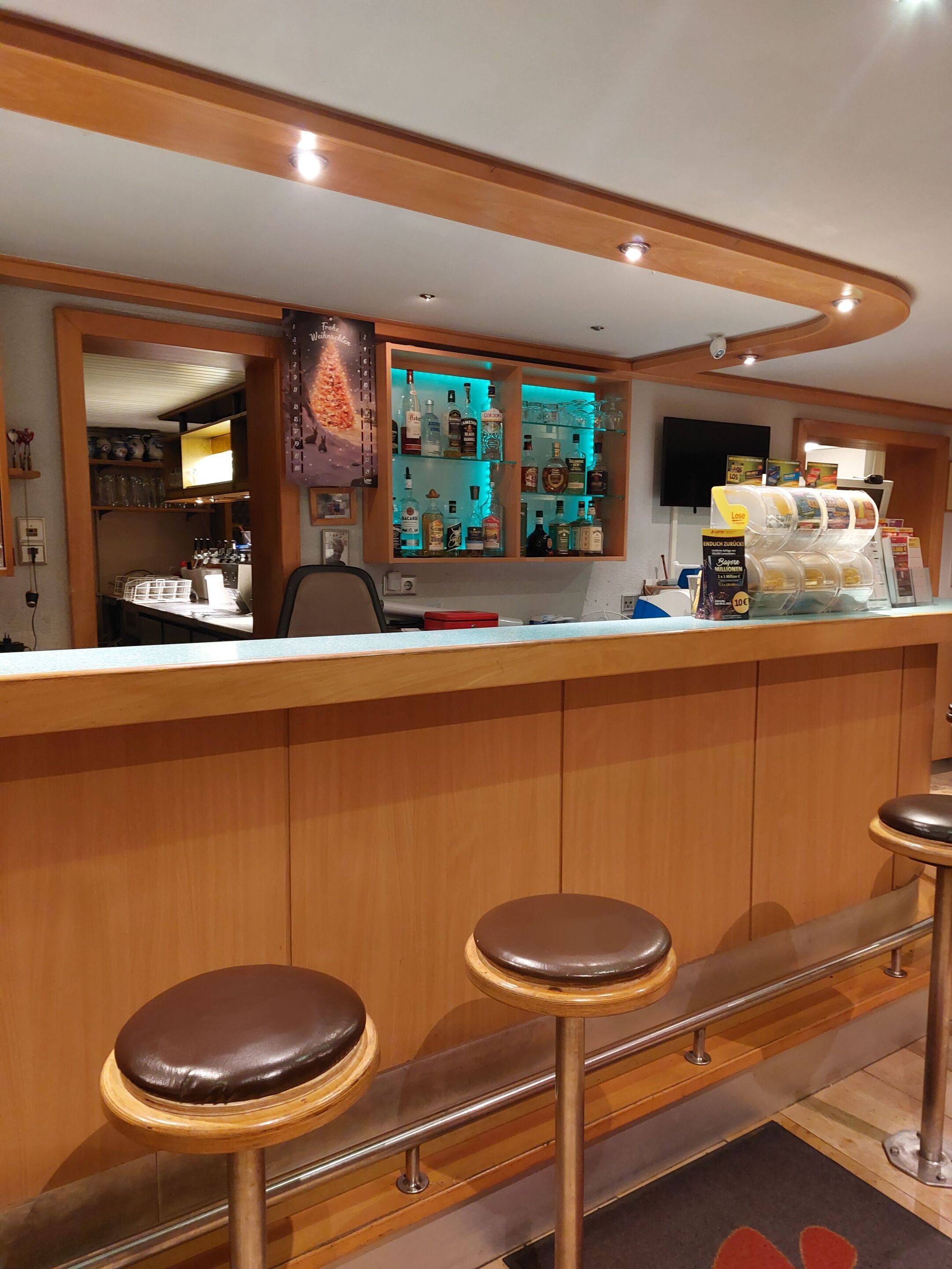 Una zona de bar con taburetes, una barra y estantes con botellas y copas.