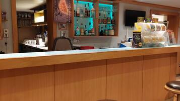 Una zona de bar con taburetes, una barra y estantes con botellas y copas.