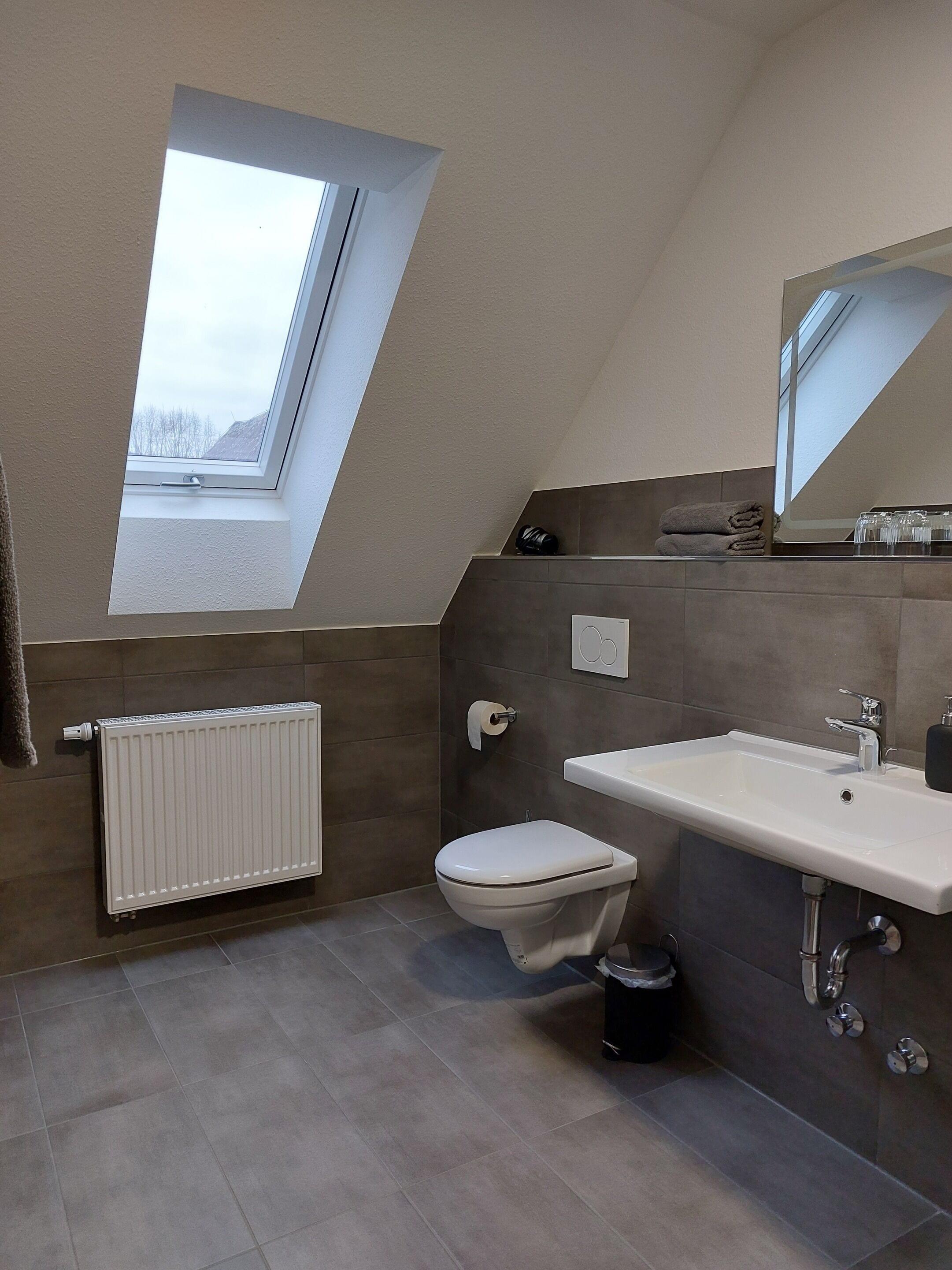 A modern bathroom with a skylight, a toilet, a sink, and a radiator.